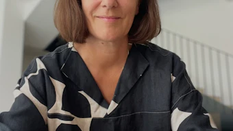 Professional portrait of a woman with shoulder-length brown hair wearing a black and white patterned shirt