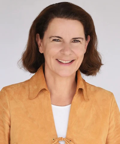 Professional headshot of a smiling woman with shoulder-length brown hair wearing a mustard-colored button-up shirt
