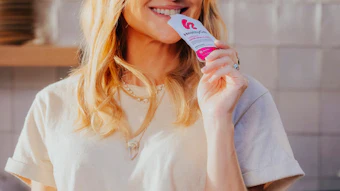 Smiling woman in white t-shirt holding pink cosmetic product in modern kitchen