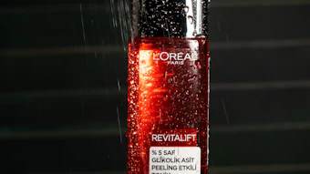 L'Oréal Revitalift glycolic acid peeling tonic bottle with water droplets under dramatic lighting