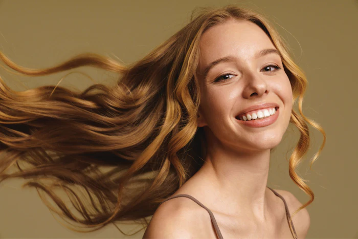 Smiling woman with flowing reddish-brown hair against a warm beige background