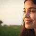 Woman smiling outdoors at sunset with blurred green field in background