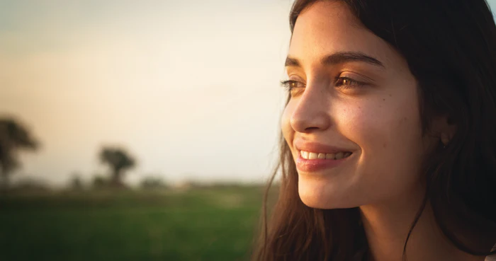 Woman smiling outdoors at sunset with blurred green field in background