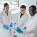 Three scientists in white lab coats conducting research with laboratory equipment and samples in a modern laboratory setting with large windows.